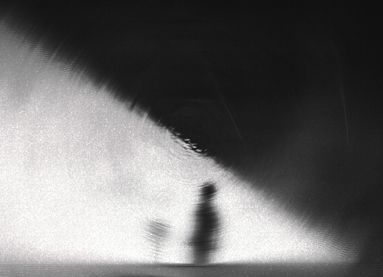 Blurred silhouette against a dramatic black and white gradient creating mystery.
